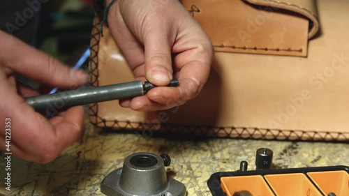Leather craftsman making at work. Close up of his hands preparing a hand rivet in order to puncture leather