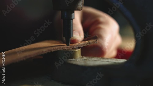 Leather craftsman at work. Close up of his hands using a hand rivet press in order to puncture leather