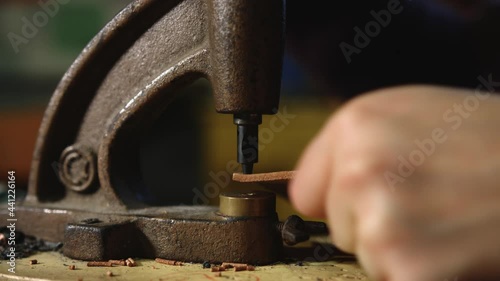 Leather craftsman at work. Extreme Close up of his hands using a hand rivet press in order to puncture leather