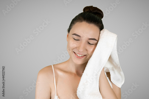 Skin care. A young woman applies a white cotton towel to her face. Gray background. High quality photo