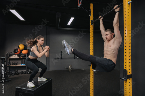 Crossfit training. Handsome shirtless muscular man doing abdominal exercise while fit sporty woman doing box jump exercise. Functional training workout, group circuit training, fitness class