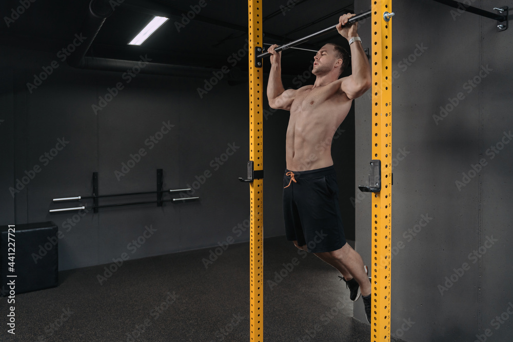 Strong young man doing pull up exercise on horizontal bar at gym ...