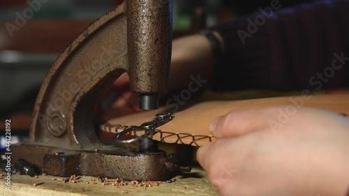 Leather craftsman at work. Close up of his hands using a hand rivet press in order to insert metal button