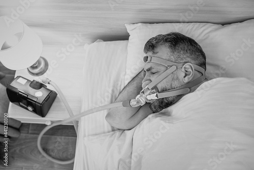 Monochrome portrait of Sleeping man with chronic breathing issues considers using CPAP machine in bed. Healthcare, Obstructive sleep apnea therapy, CPAP, snoring concept photo