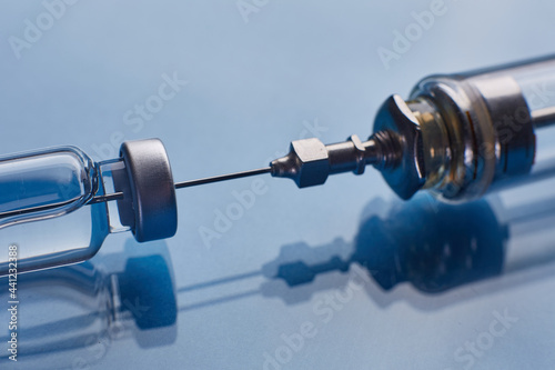 Glass vaccine vial and glass syringe on blue glass background
