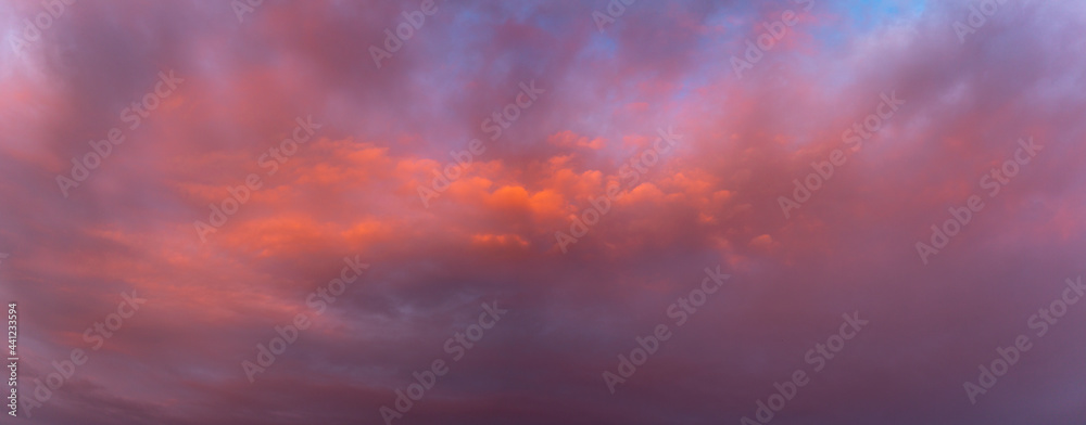 Dispersion clouds in front of dramatically lit cloud showing texture and detail brightly colorful orange at sunset with blue tints in the background. 