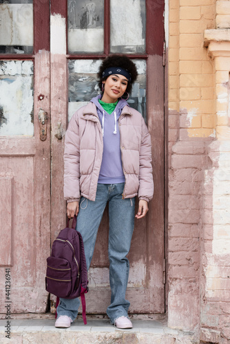 African american woman with backpack standing near old building with wooden door