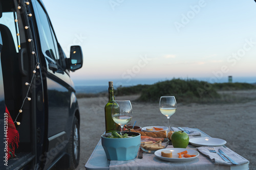Camping table with wine and food next to van facing the sea