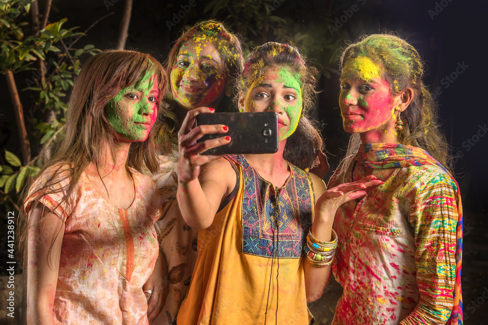 Group of happy young girls having fun and taking selfie using smartphone on Holi festival. Festival and technology concept