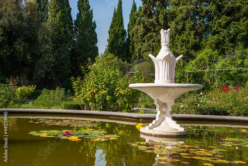 Fountain in a pool with lilies on the background of coniferous forest.