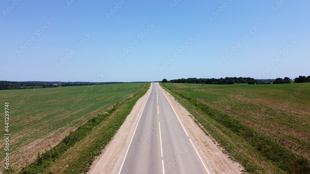 The road along the green fields. Landscapes on a sunny day. The road is visible from the air. Landscape from a bird's eye view. Aerial photography. 