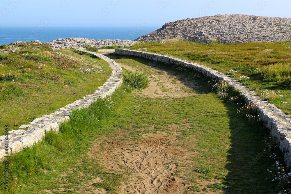 A low stone wall lined curving path through public land next to the sea Suances Cantabria Spain May 2021