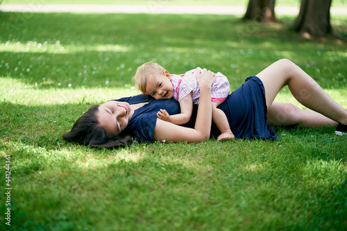 Mom lies with a little girl on her stomach on a green lawn