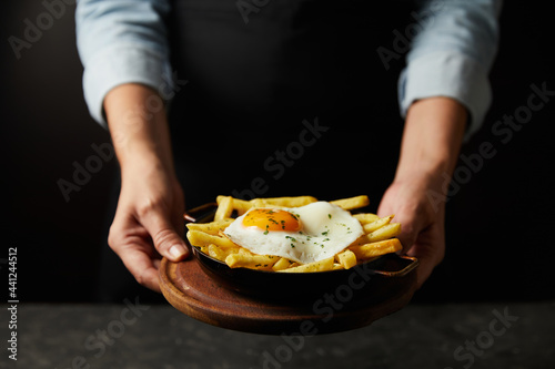 young woman hands serving french fries portion with fried egg on top