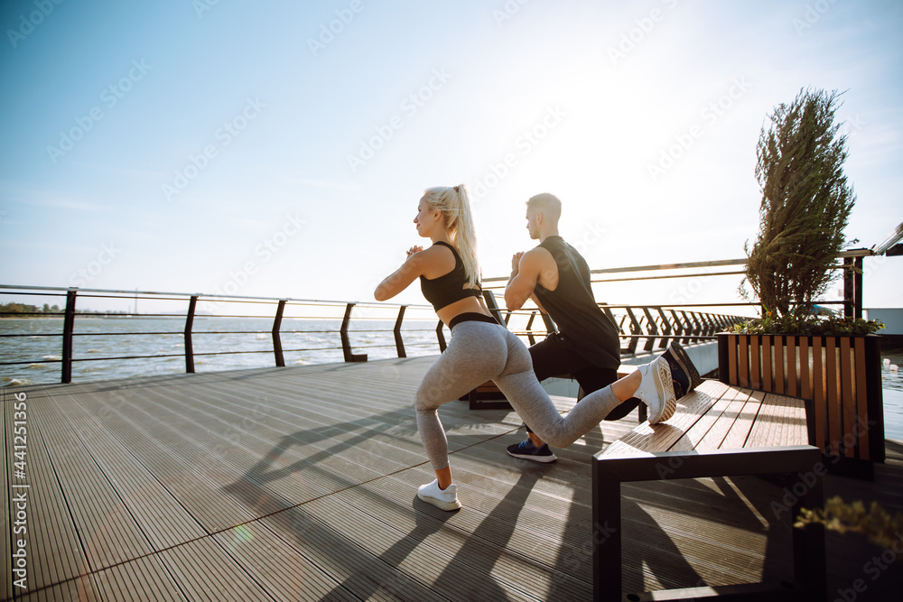 Young fitness couple is doing workout at the beach pier. Young man and woman doing exercises outdoors in the morning. Sport, Active life. 