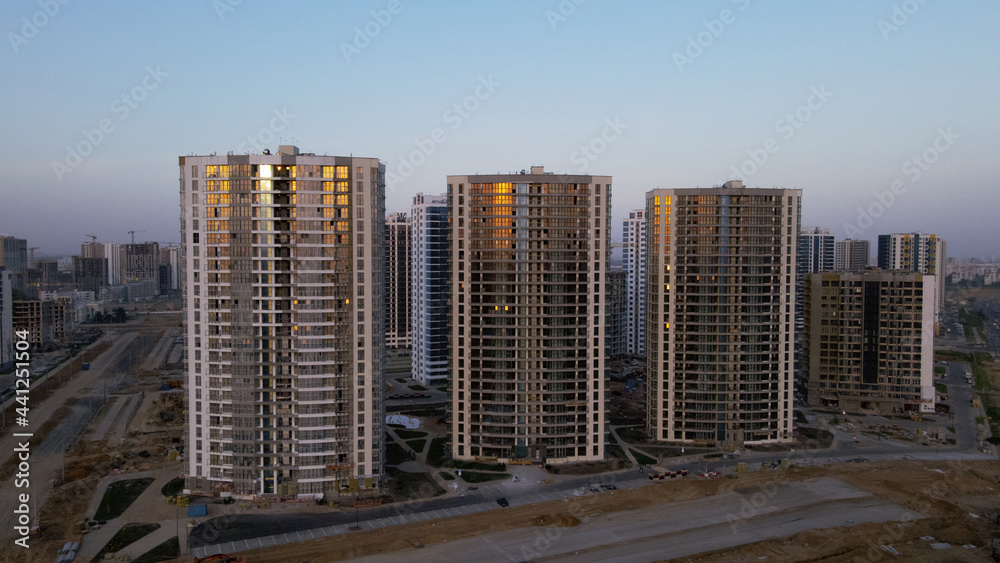 Construction of a new city block. New construction of modern multi-storey buildings. The setting sun is reflected in the windows of the houses. Aerial photography.