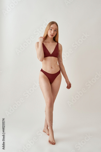 Full length shot of attractive young slim caucasian woman with fit body wearing burgundy underwear looking at camera, posing isolated over light gray background