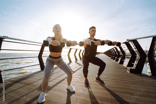 Young fitness couple is doing workout at the beach pier. Young man and woman doing exercises outdoors in the morning. Sport, Active life.  © maxbelchenko