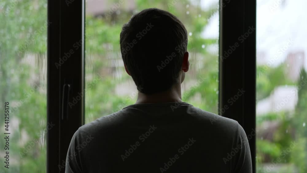 Silhouette of a man looks outside the window at the rain Silhouette of a man looks outside the window at the rain