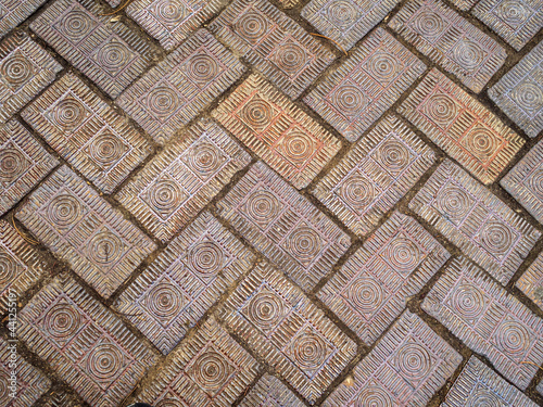 Old worn decorative brick pavers with intricate carved design. Medium close view.