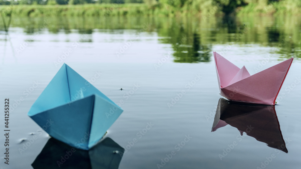 Two paper boats of red and blue color, floating on the water. Summer day on the river bank. Playing with paper boats. 4K