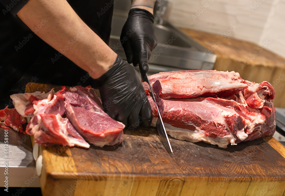 Butcher cuts the meat with a knife on a wooden board. Cutting and preparation of farm meat products