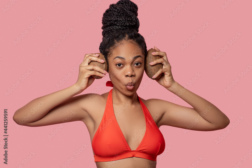 Fototapeta premium Dark-skinned woman holding coconuts and looking enjoyed