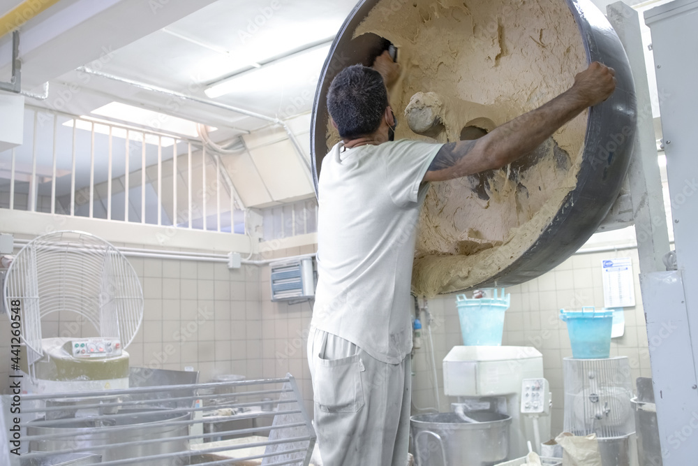Baker takes dough with bread from kneading machine. Concept of production of bread and flour products at industrial level, in large quantity Baker takes dough with bread from kneading machine. Concept of production of bread and flour products at industrial level, in large quantity