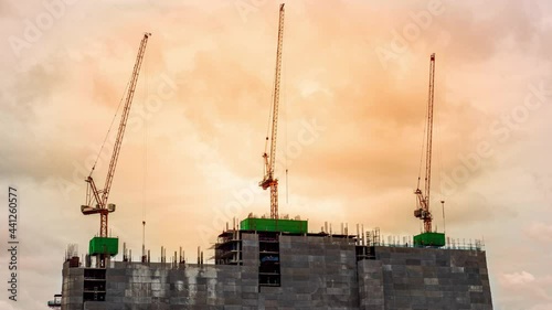 Time-lapse footage of High crane works on building site with view of a skyscrapers, sky evening on a background. Many construction workers are working and controlling the crane.