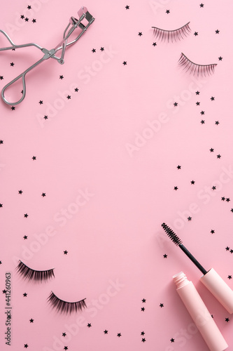 Фотография Frame of mascara, false eyelashes, curler and confetti on pink background
