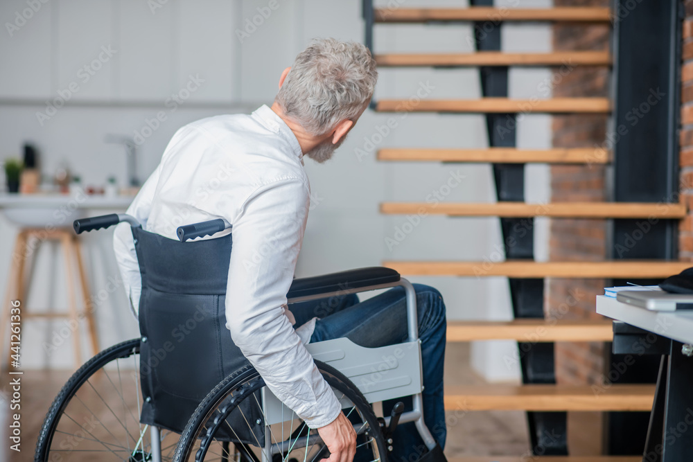 Handicapped gray-haird man in white shirt and jeans at home