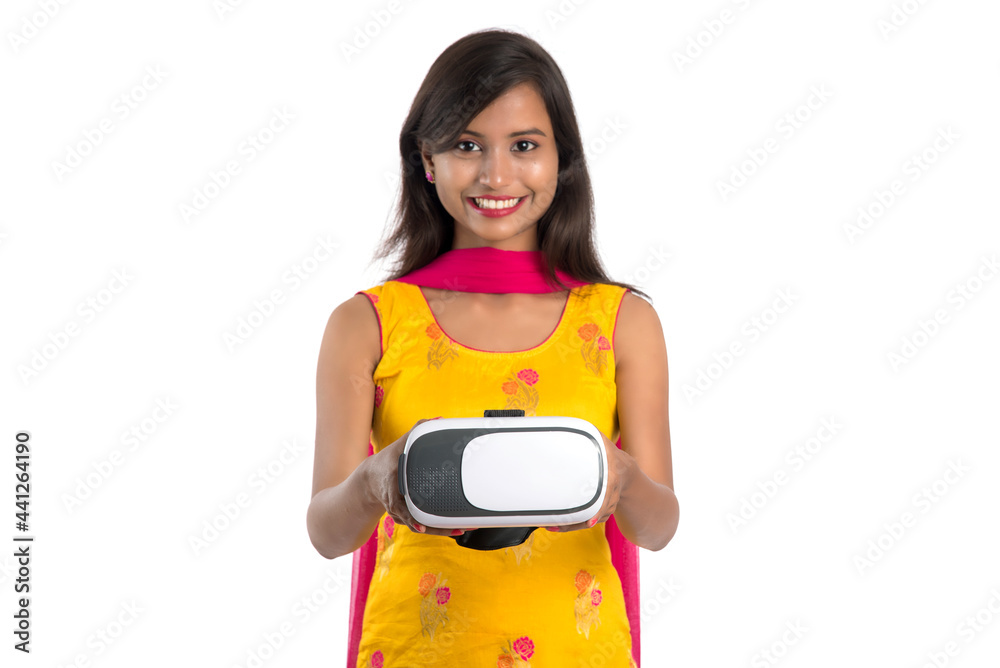 Indian traditional young girl holding and showing VR device, vr box, goggles, 3D Virtual Reality Glasses headset, Girl with Modern imaging Future technology on white background. Indian traditional young girl holding and showing VR device, vr box, goggles, 3D Virtual Reality Glasses headset, Girl with Modern imaging Future technology on white background.