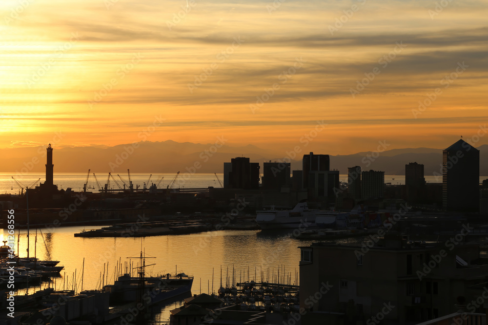 Romantic sunset with panoramic view of Genoa city with its harbour, the silohuettes of skycrapers and the majestic lighthouse (Lanterna) symbol of the Italian city.