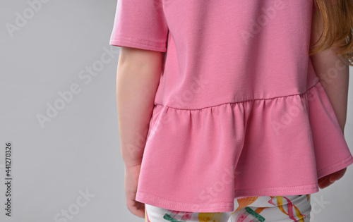 back view of a detail of children's summer wardrobe - a pink cotton T-shirt with a short sleeve and a peplum, and colorful legends.
