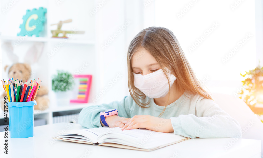 Cute schoolgirl in medical face mask studying at home