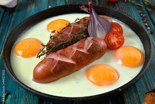 breakfast with fried eggs and sausages on pan, onion, herbs, tomatoes and garlick on wooden background closeup