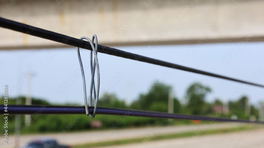 Metal wire to hold the cable. Electrical wires bound with anti-sagging wire on blurry green tree background. select focus Metal wire to hold the cable. Electrical wires bound with anti-sagging wire on blurry green tree background. select focus