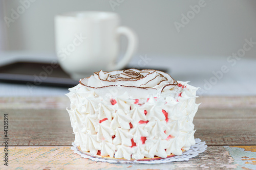 Mini vanilla cake decorated with dried coconut chips and whipped cream. In the background, a blurred cup of coffee.