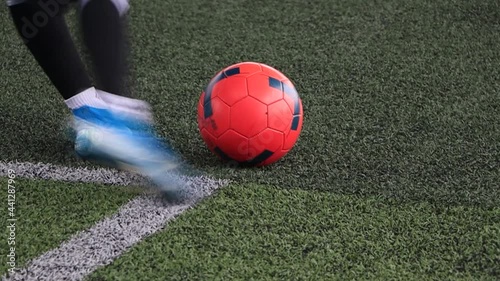 close up An orange soccer ball on a green grass is being kicked out slow motion