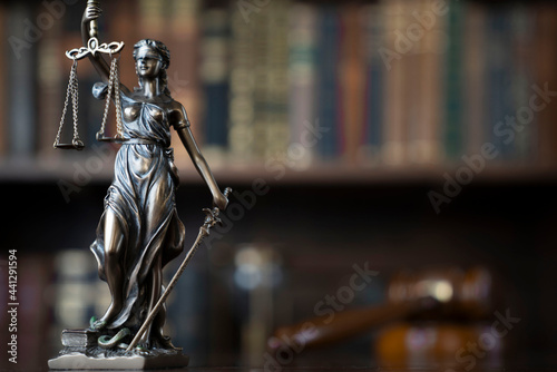 Law theme. Judge chamber. Themis and gavel on brown shining desk. Collection of legal books in the bookshelf.