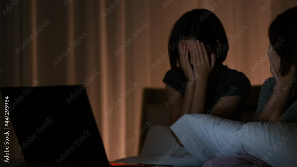 Two Asian girl watch scary movie on bed and they use hands to cover face and eye in the scene of horror. Two Asian girl watch scary movie on bed and they use hands to cover face and eye in the scene of horror.