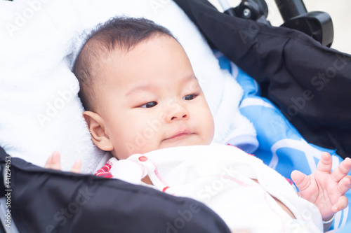 Asian baby boy wakes up from his nap in his baby carriage outdoors. Family leisure with little child. photo