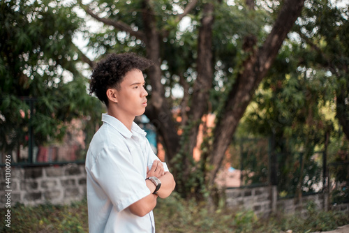 An upset young Blasian man with hands crossed while outdoors. Feeling down after a petty argument. Teenage angst and strong emotion concept.