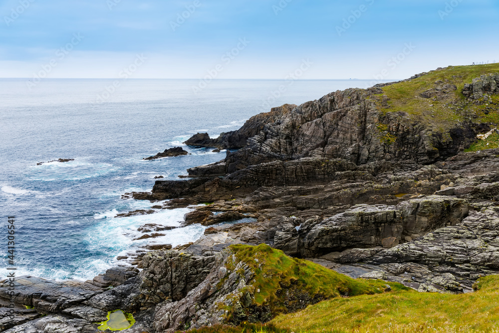 Rugged landscape at Malin Head, County Donegal, Ireland. Rough beach with cliffs, green rocky land with sheep on foggy cloudy day.