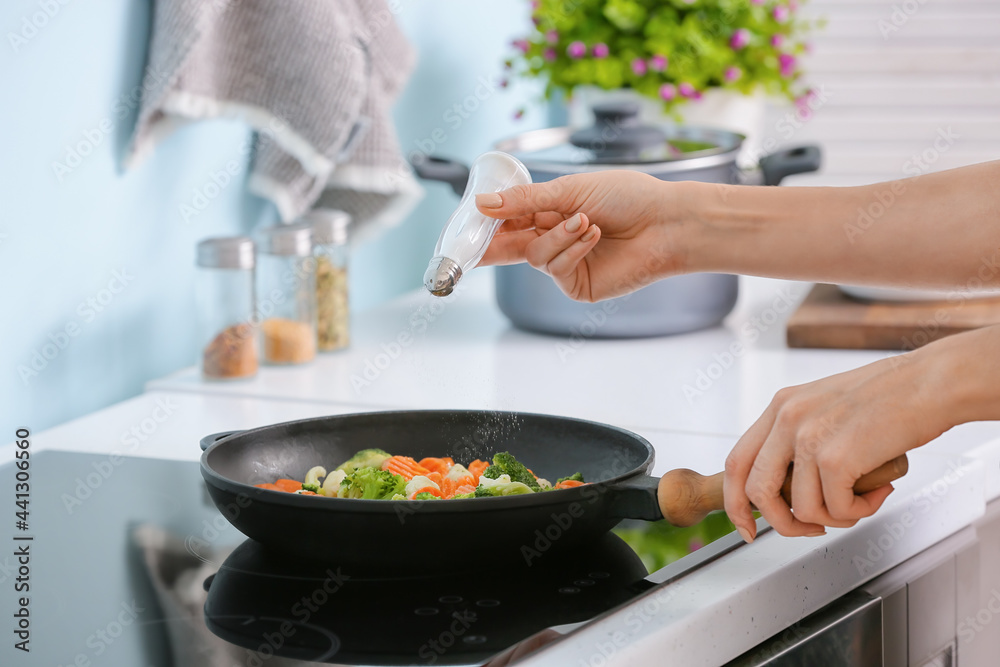 Woman preparing vegetables on electric stove in kitchen