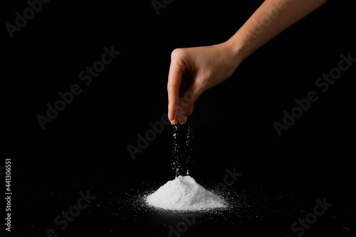 Woman sprinkling salt on dark background, closeup photo