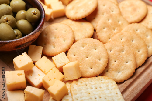 Board with tasty crackers, cheese and olives, closeup