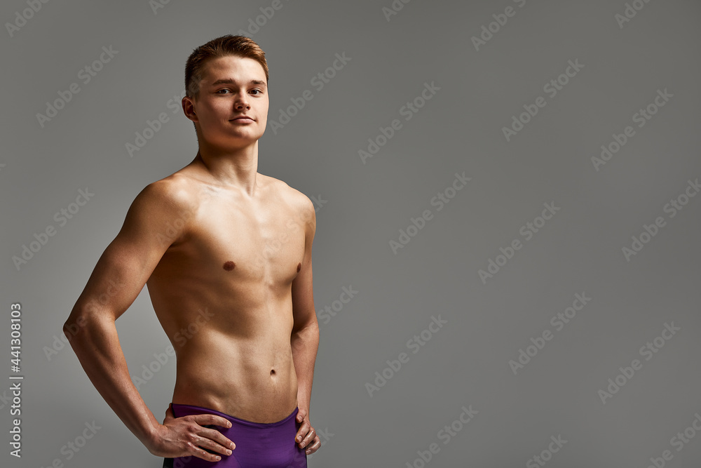 Young athlete swimmer in excellent physical shape looks at the camera, half-length portrait on a gray background, copy space, motivation for sports, advertising banner.