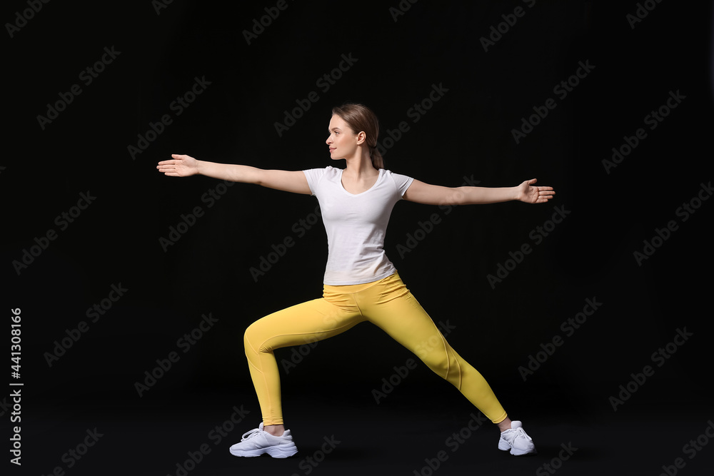 Sporty young woman doing yoga on dark background