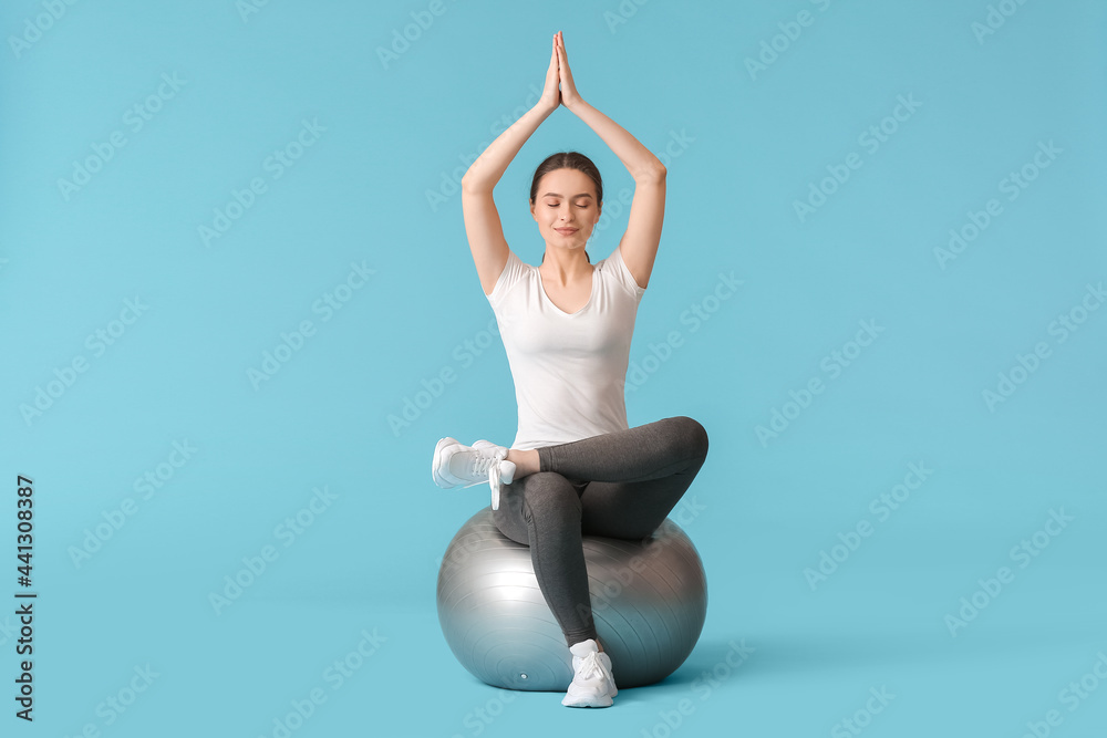 Sporty young woman with fitball doing yoga on color background